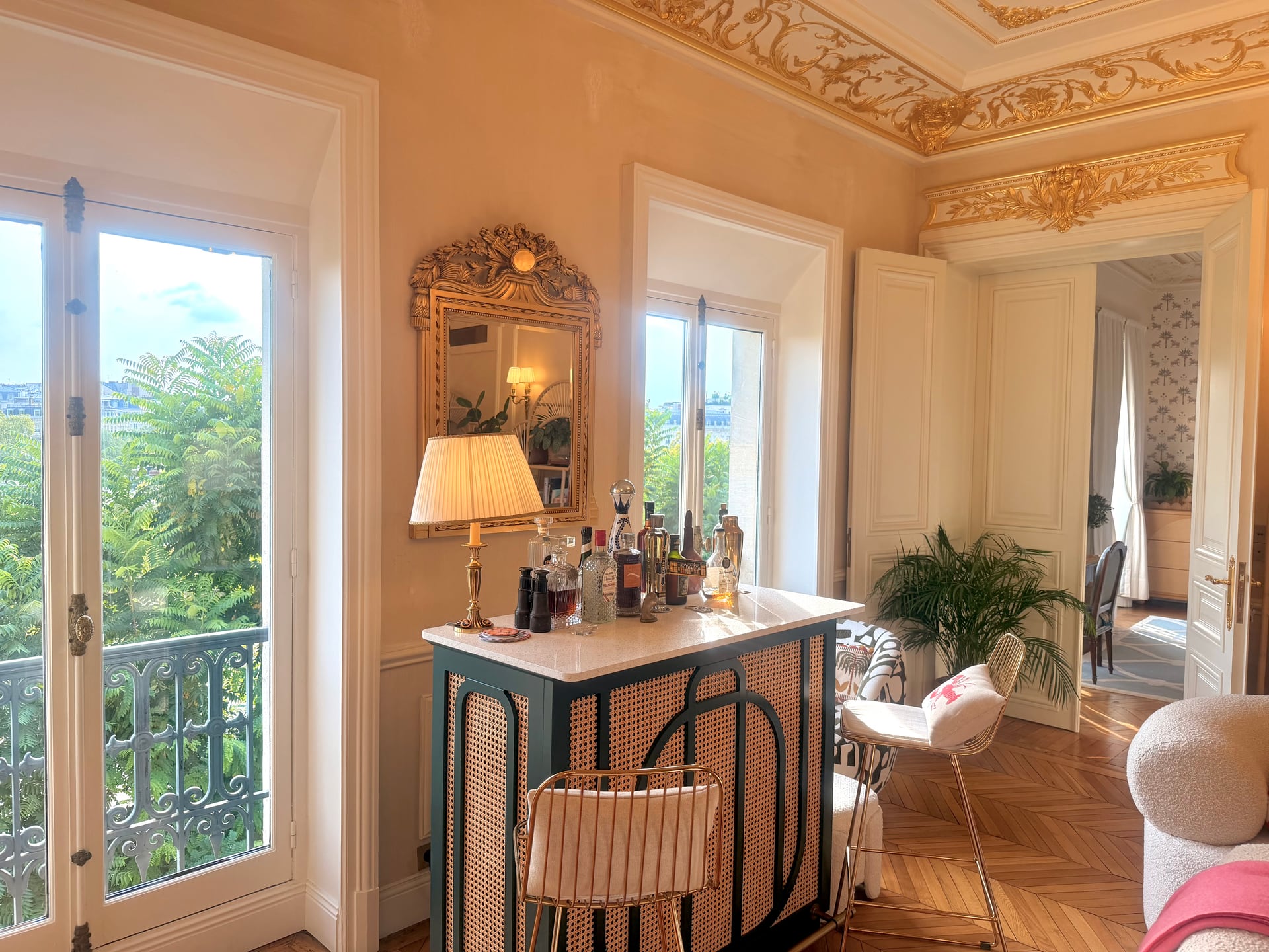 The cane bar and gold mirror by the balcony door, lamps lit